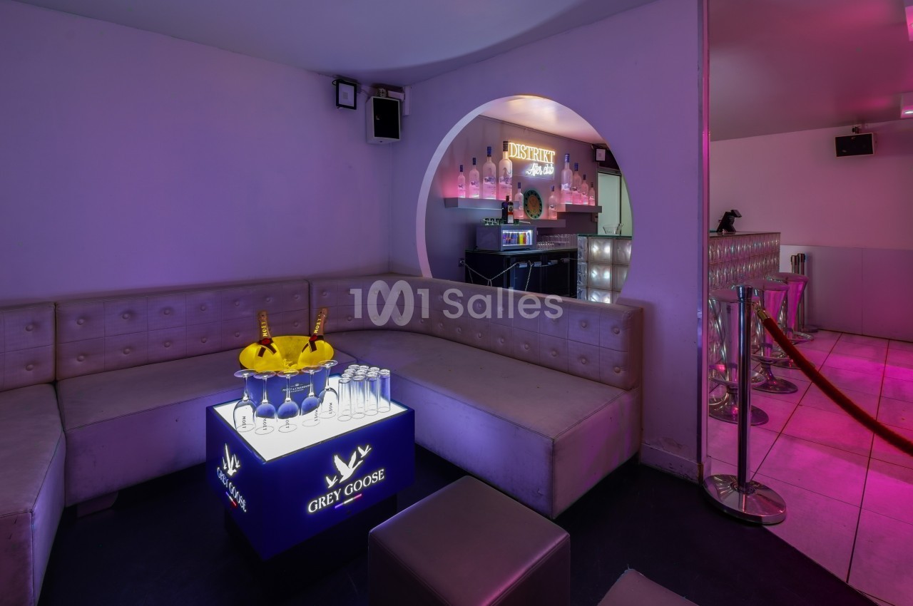 Banquette en cuir beige dans un lounge avec table lumineuse, seaux à champagne et bar éclairé en arrière-plan.