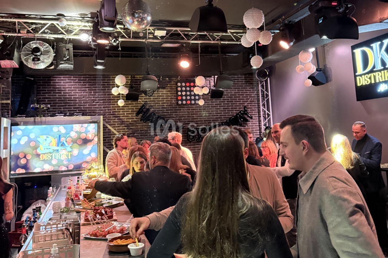 Des personnes rassemblées dans un bar ou restaurant, discutant et se servant à un buffet sous une décoration lumineuse.