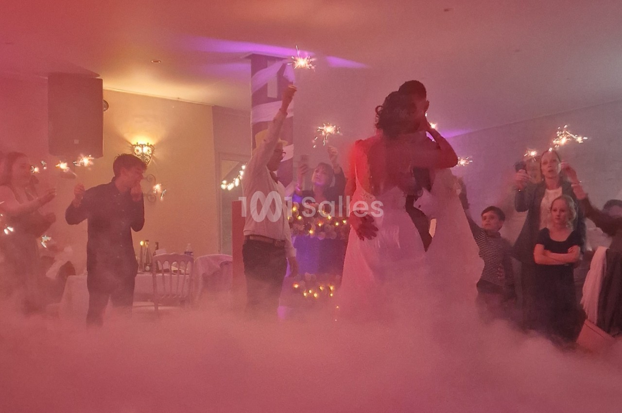 Un couple danse dans une salle éclairée de lumières tamisées, entouré d'invités tenant des cierges magiques.