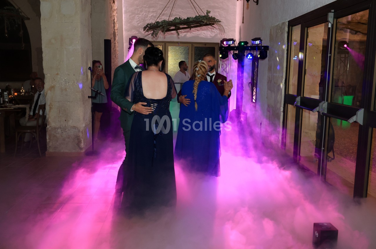 Deux couples dansent sur une piste entourée de fumée et éclairée par des lumières colorées dans une salle en pierre.