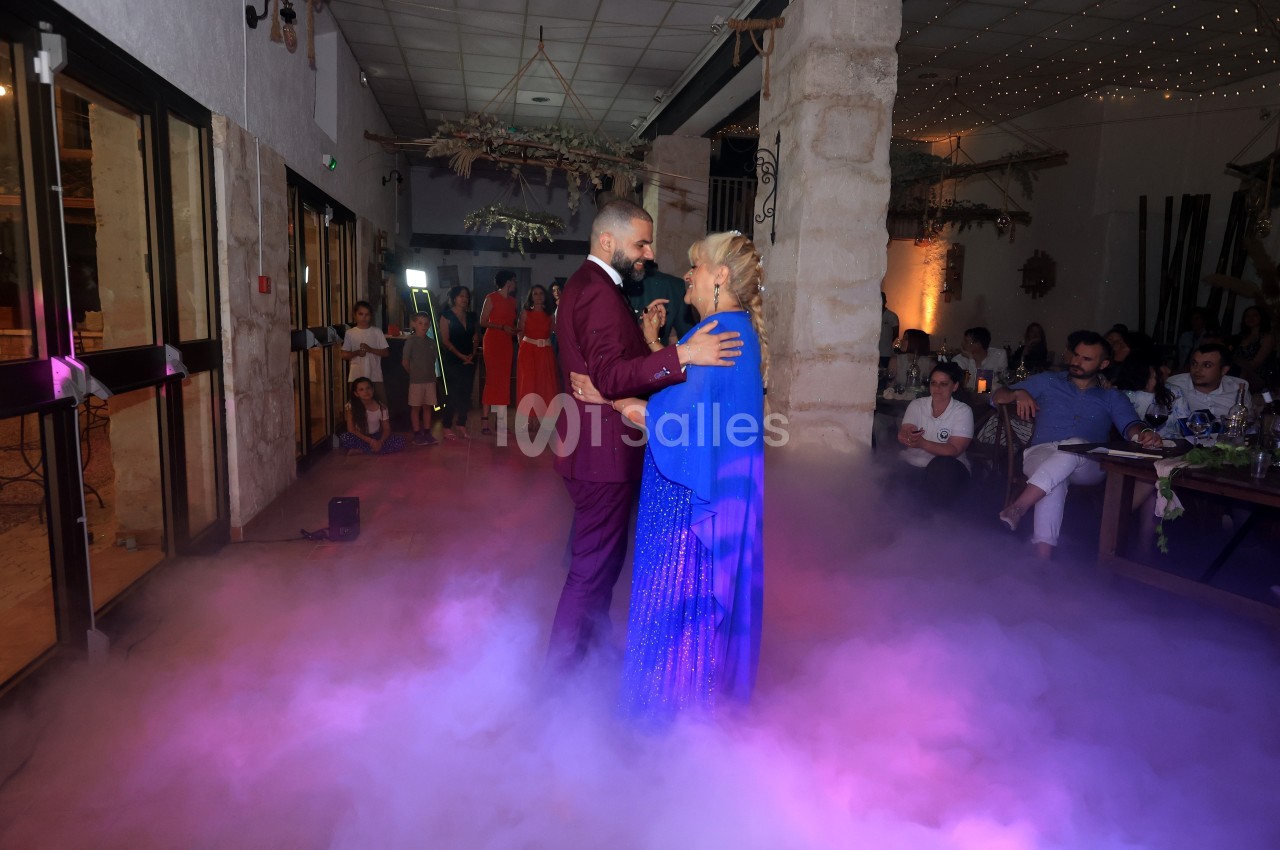 Un couple danse au milieu d'une piste entourée de fumée, sous un éclairage tamisé dans une salle festive.