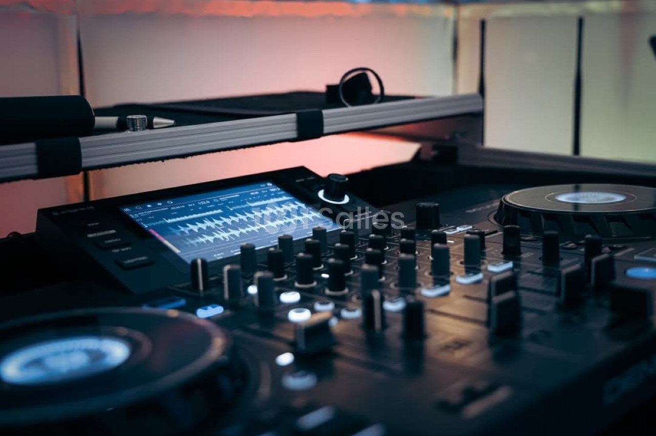 Table de mixage avec platines et écran affichant des ondes sonores, éclairée par une lumière tamisée.
