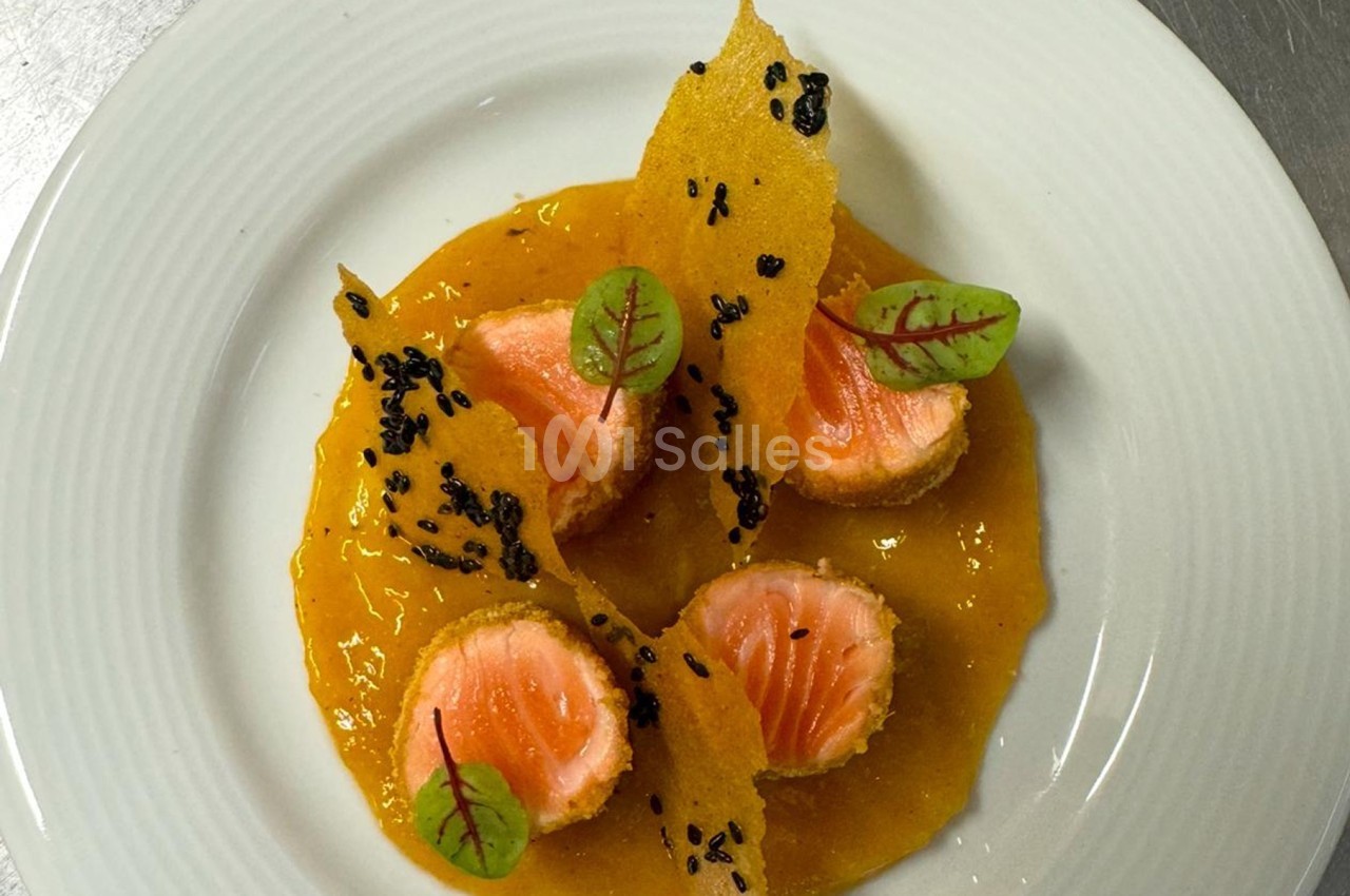 Assiette gastronomique avec des morceaux de saumon en croûte, sauce orange, feuilles décoratives et éclats noirs.