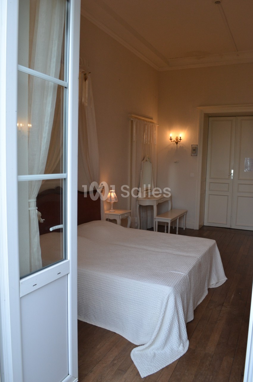 Chambre lumineuse avec lit double, parquet en bois, mobilier blanc et éclairage mural chaleureux.