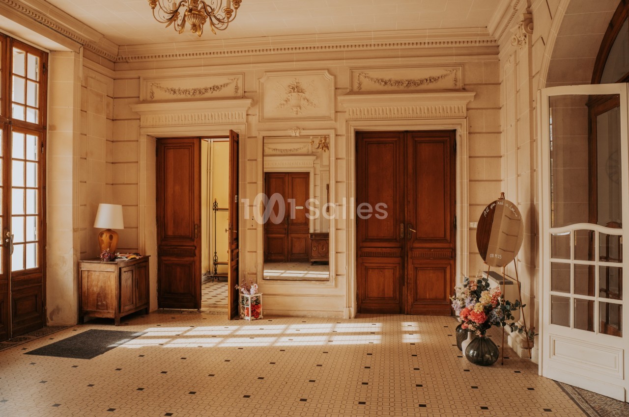 Hall d'entrée lumineux avec carrelage ancien, portes en bois, miroir mural et décoration florale.