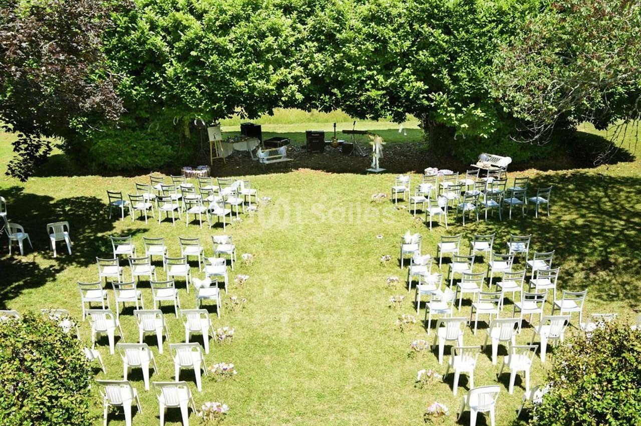 Chaises blanches disposées en rangées sur une pelouse, formant une allée centrale, avec des arbres en arrière-plan.