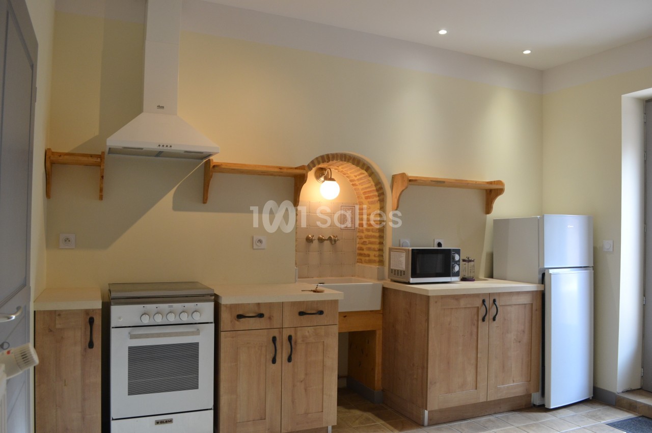 Cuisine équipée avec meubles en bois, évier, cuisinière, hotte, micro-ondes, réfrigérateur et éclairage mural.