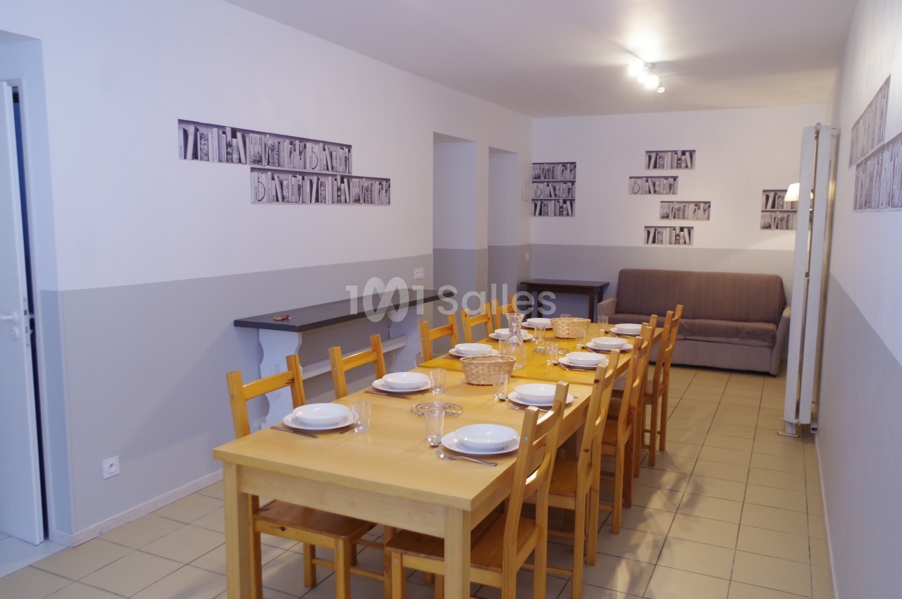 Salle à manger avec une grande table en bois, chaises assorties, vaisselle disposée et un canapé en arrière-plan.