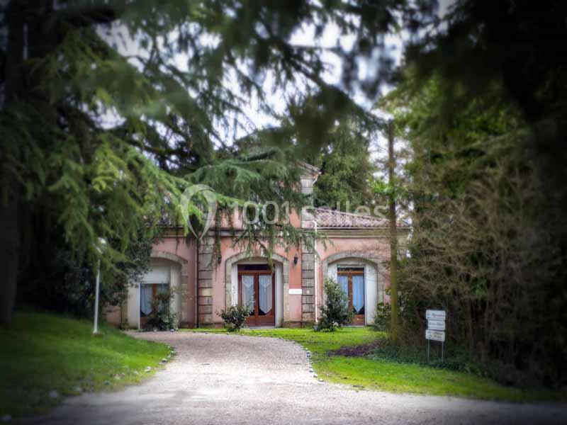 Façade d'une maison rose entourée d'arbres, avec une allée en gravier menant à l'entrée.