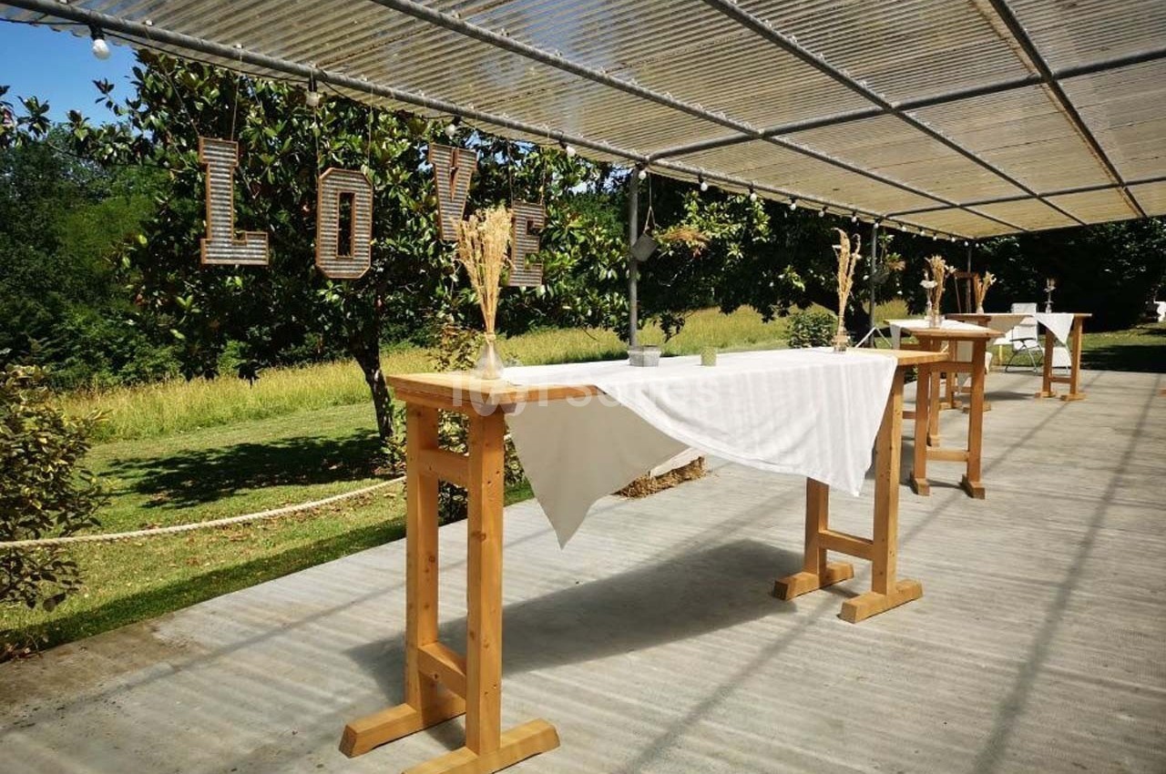 Tables en bois décorées de nappes blanches et de bouquets, sous une pergola avec le mot ’LOVE’ suspendu.
