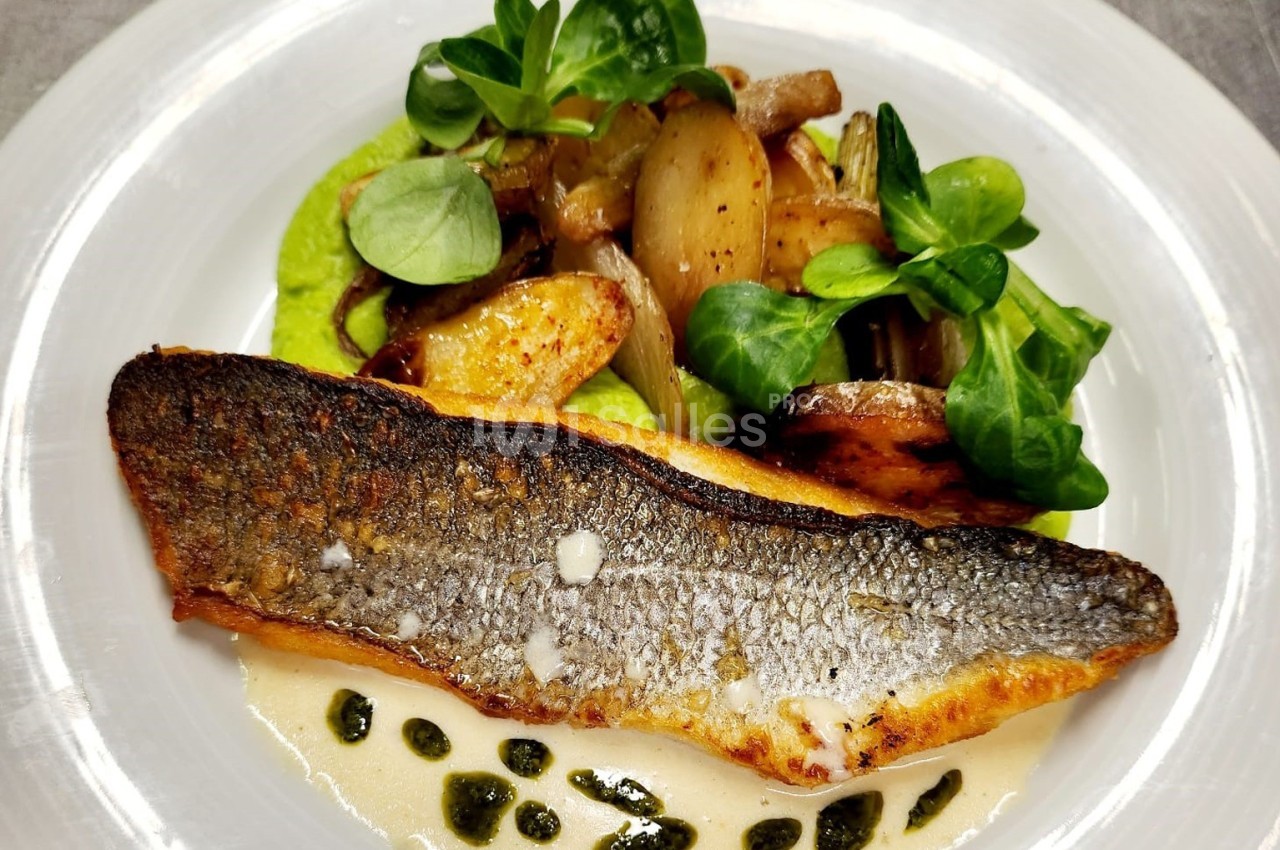 Filet de poisson grillé servi avec purée verte, pommes de terre rôties, oignons caramélisés et feuilles de mâche.