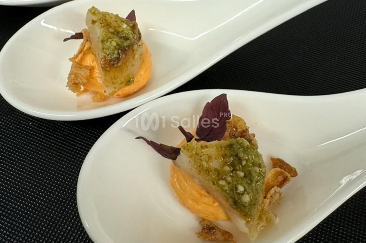 Deux cuillères en porcelaine contenant une bouchée de poisson, crème orange, herbes et éclats croustillants.