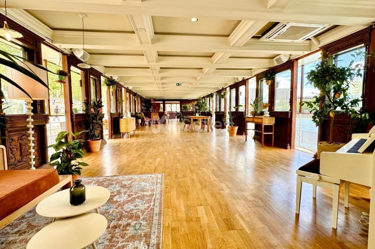 Salle lumineuse avec parquet, grandes fenêtres, plantes décoratives et mobilier en bois clair.