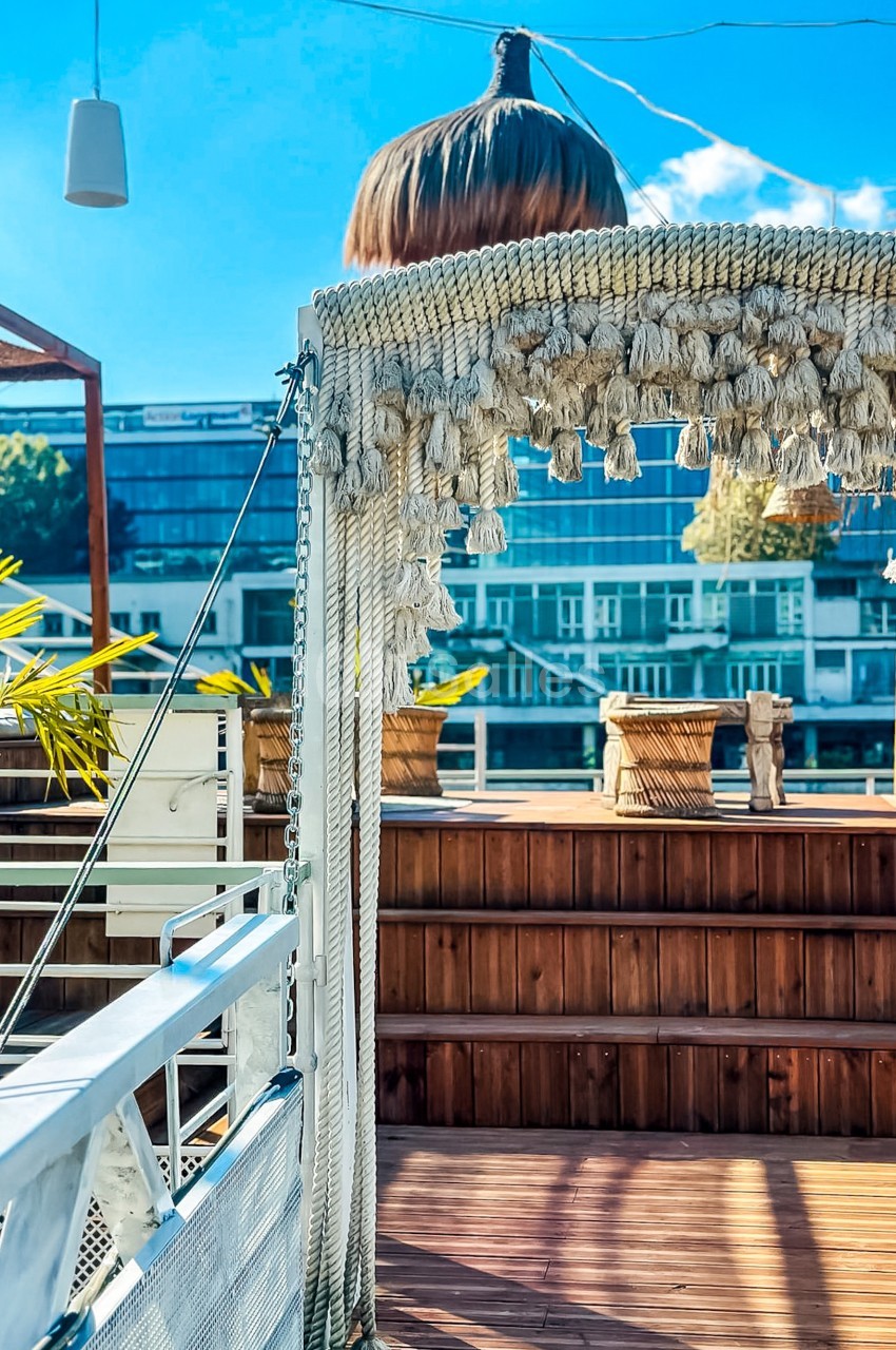 Terrasse en bois avec une arche décorative en corde, entourée de plantes et surplombant des bâtiments modernes.