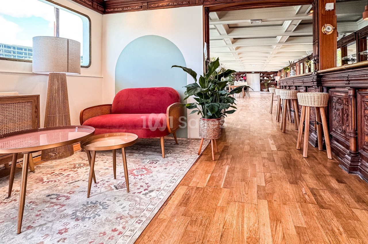 Salon lumineux avec canapé rouge, tables basses, plante verte et parquet, dans un espace au décor boisé et raffiné.