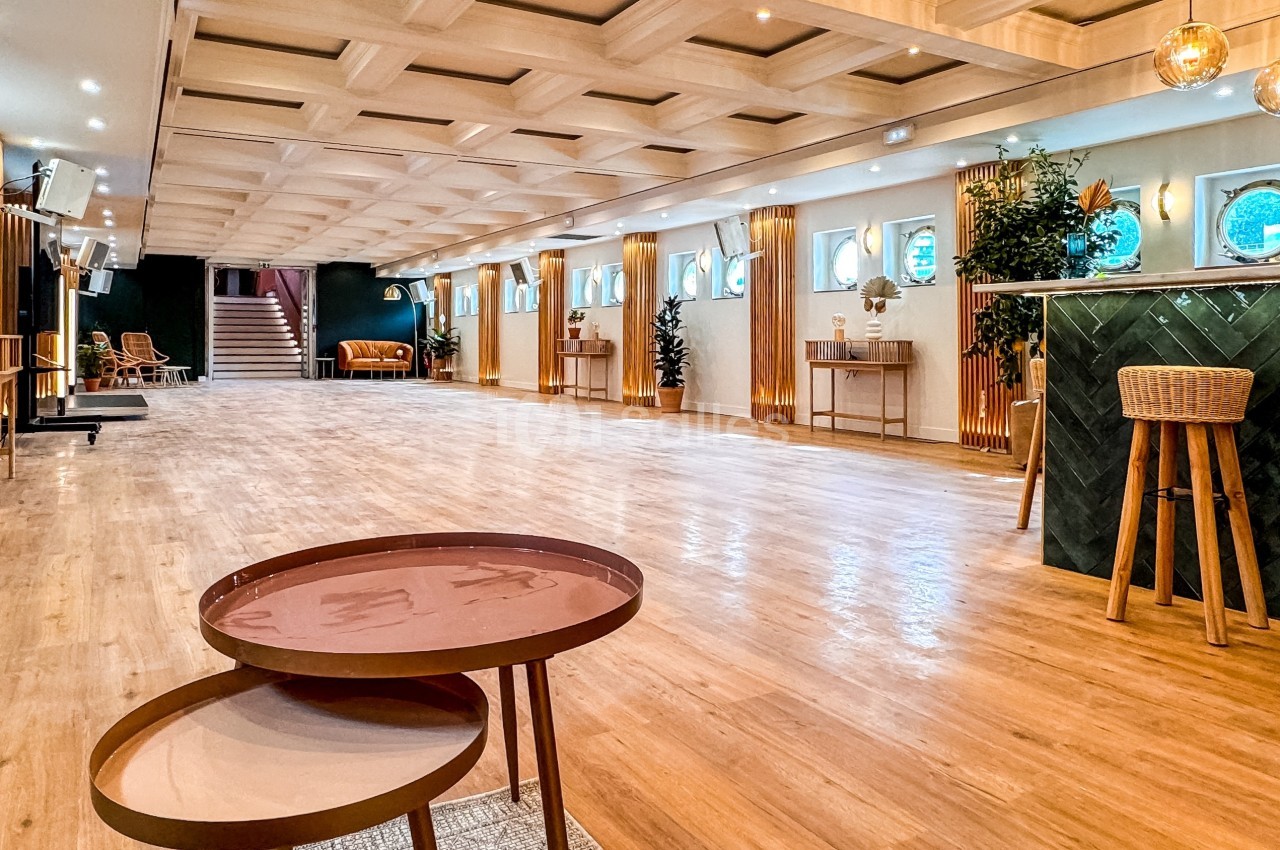 Salle spacieuse avec parquet clair, mobilier moderne, bar vert et éclairage chaleureux.