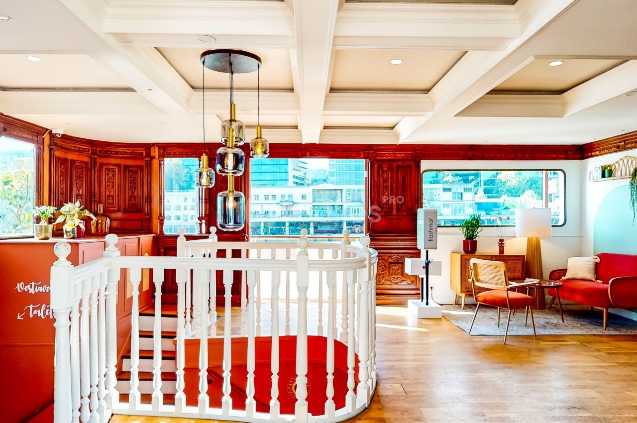 Intérieur lumineux avec escalier blanc central, mobilier en bois, fauteuils rouges et grandes fenêtres donnant sur l…
