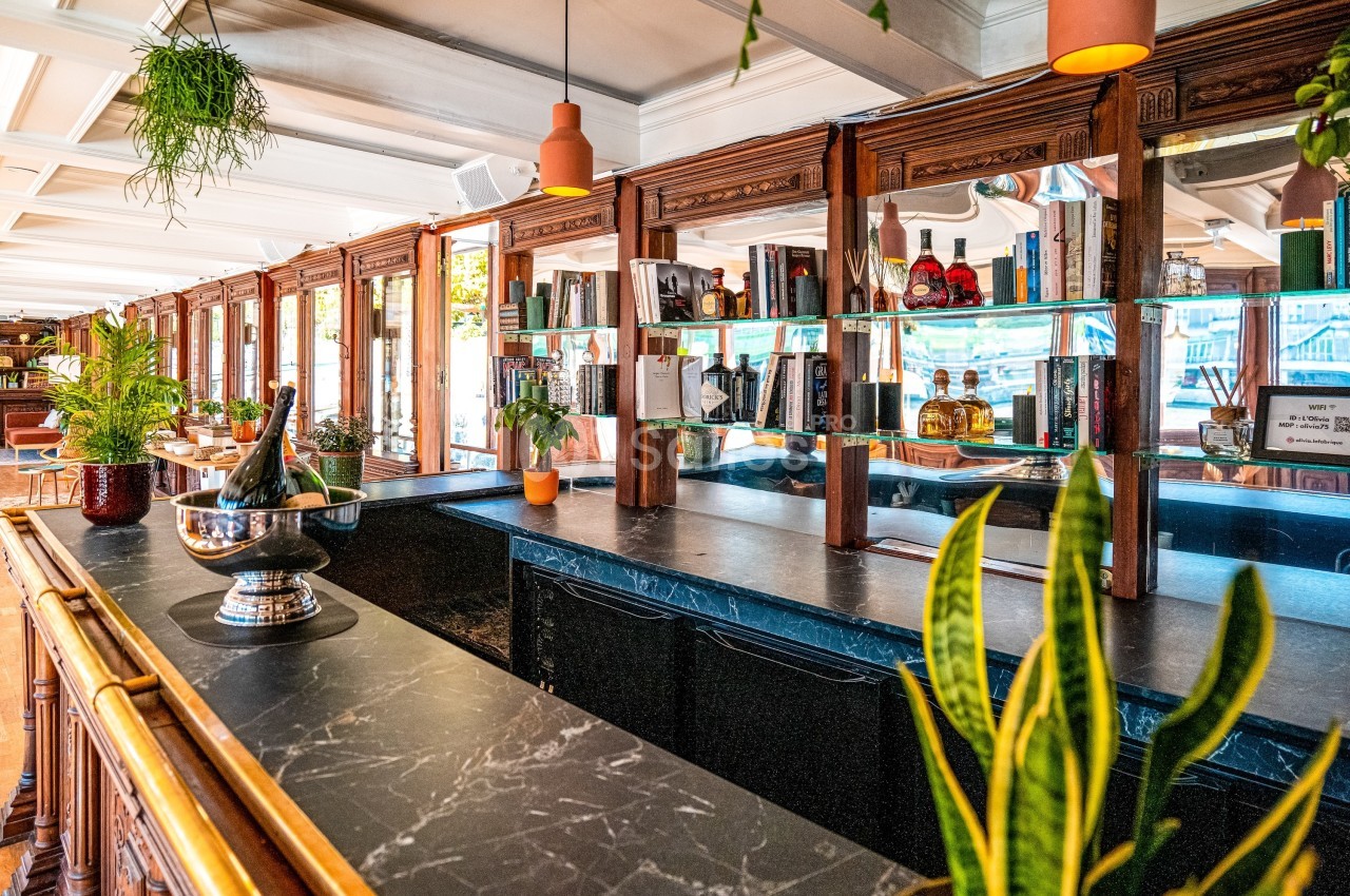 Bar en bois avec comptoir en marbre noir, décoré de plantes et de bouteilles, dans un espace lumineux.