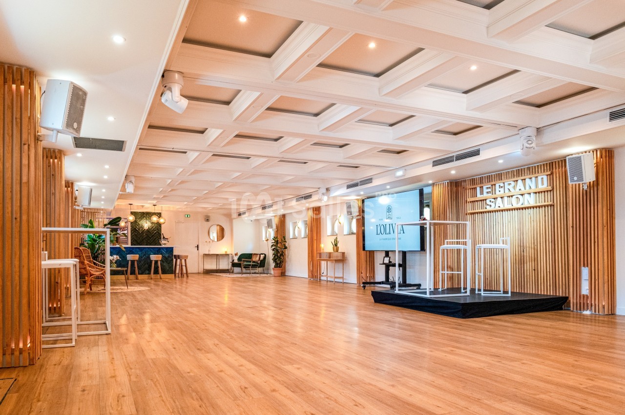 Salle lumineuse avec parquet, plafond à caissons, estrade, mobilier moderne et éclairage intégré.