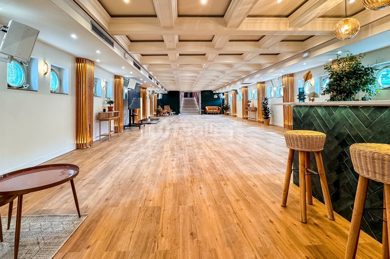 Salle spacieuse avec parquet clair, bar en bois et décoration moderne, éclairée par des luminaires suspendus.