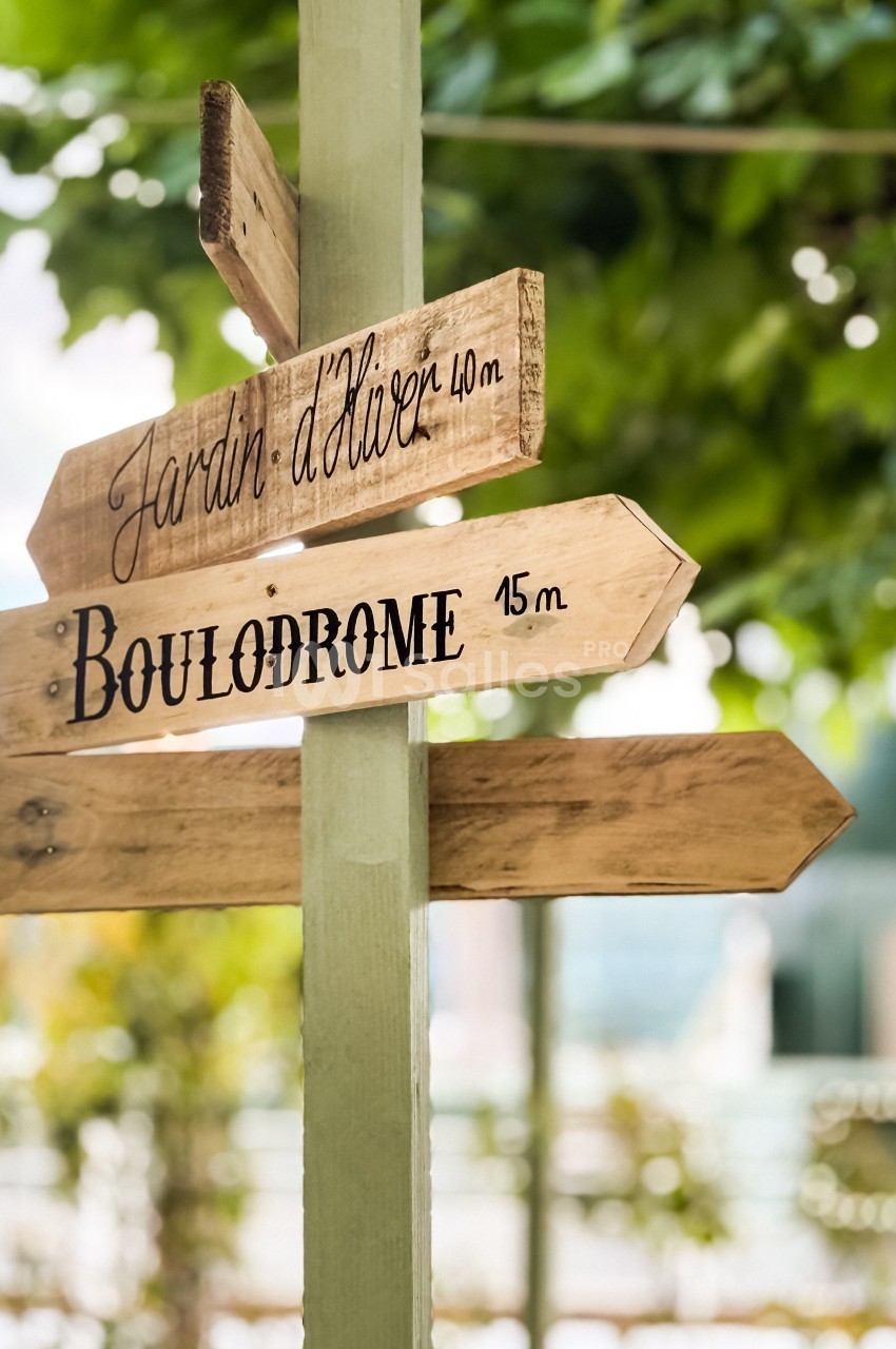 Panneau en bois indiquant les directions vers un jardin d'hiver et un boulodrome, entouré de verdure.