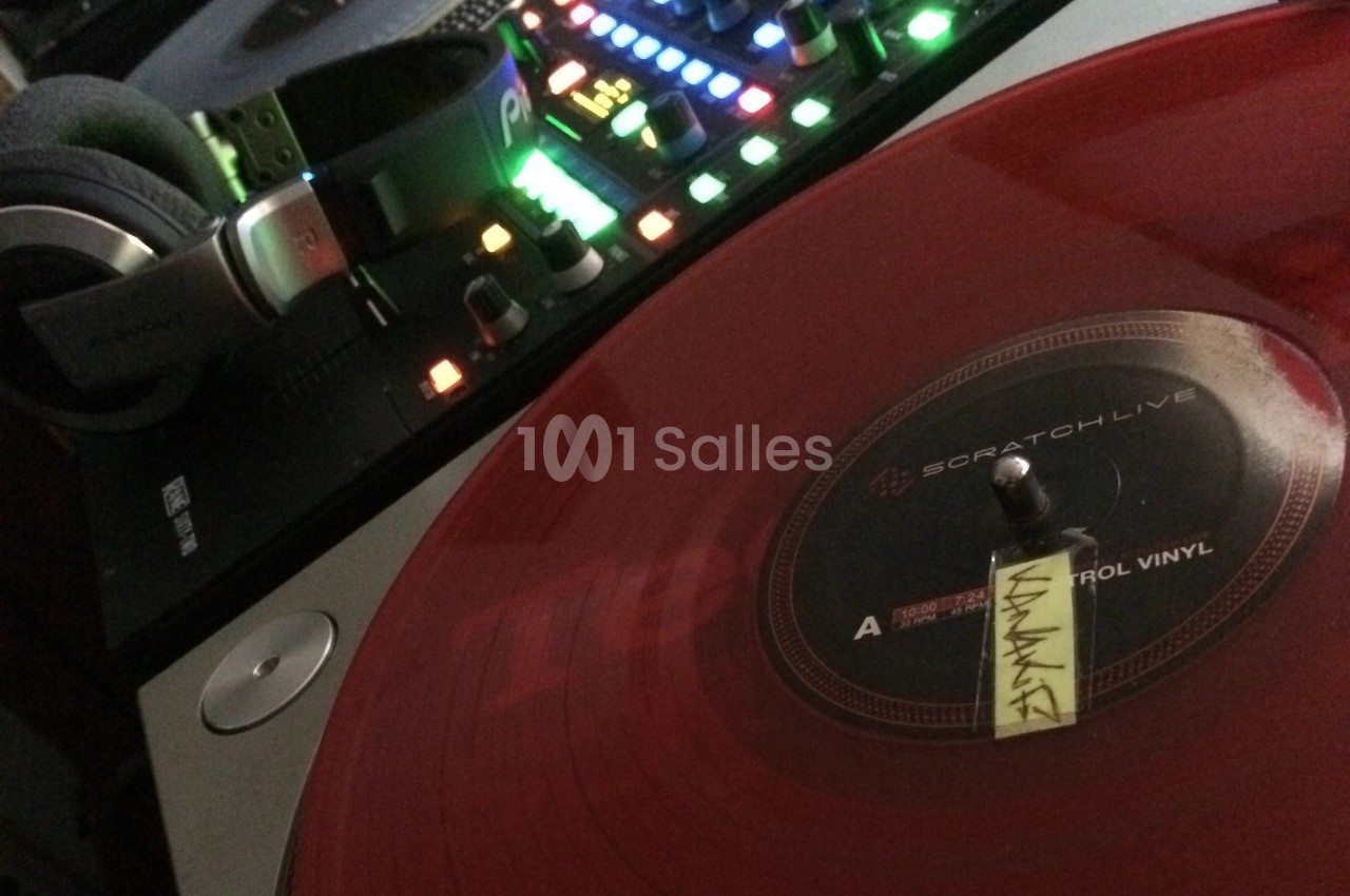 Platine vinyle rouge en lecture avec casque audio posé à côté et table de mixage lumineuse en arrière-plan.