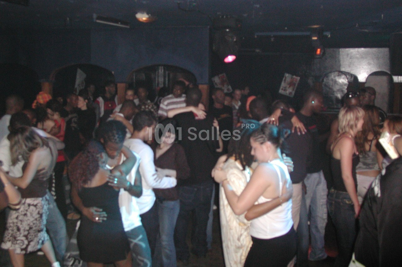 Personnes dansant en couple dans une salle sombre, ambiance festive avec plusieurs groupes rapprochés.
