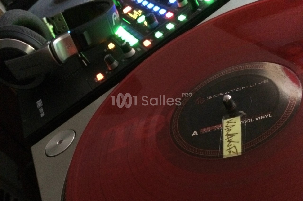 Platine vinyle avec disque rouge translucide en lecture, casque audio et table de mixage rétroéclairée en arrière-plan.
