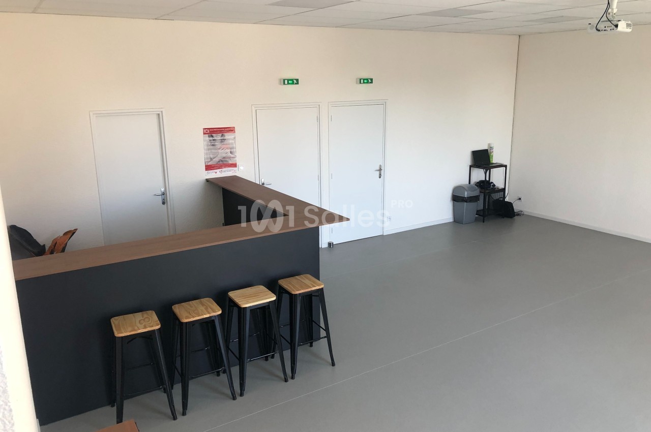 Salle lumineuse avec un comptoir en bois, quatre tabourets hauts, trois portes blanches et un coin avec ordinateur et…