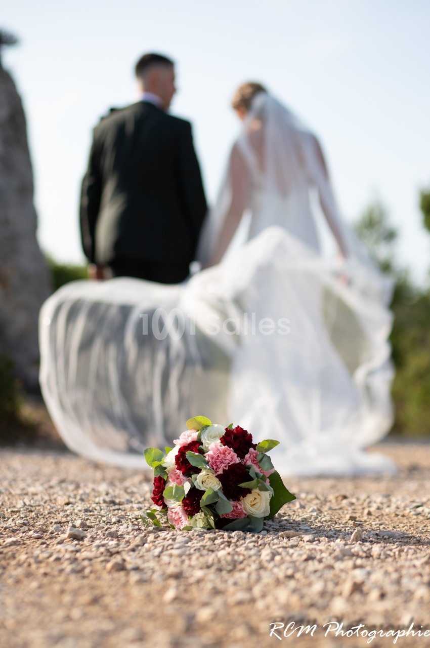 Un bouquet de fleurs posé au sol avec un couple de mariés flou en arrière-plan.