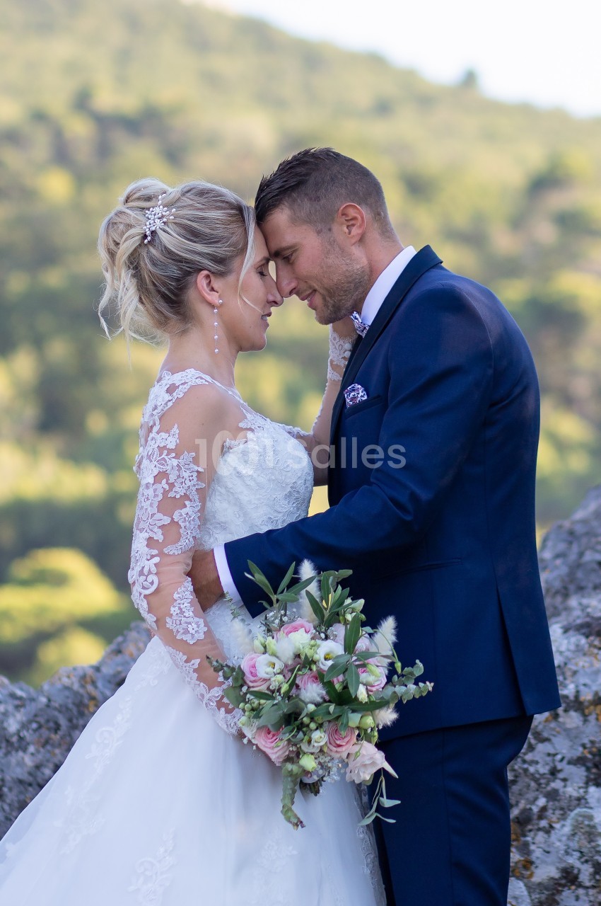 Un couple en tenue de mariage se tient tendrement face à face dans un cadre naturel verdoyant.