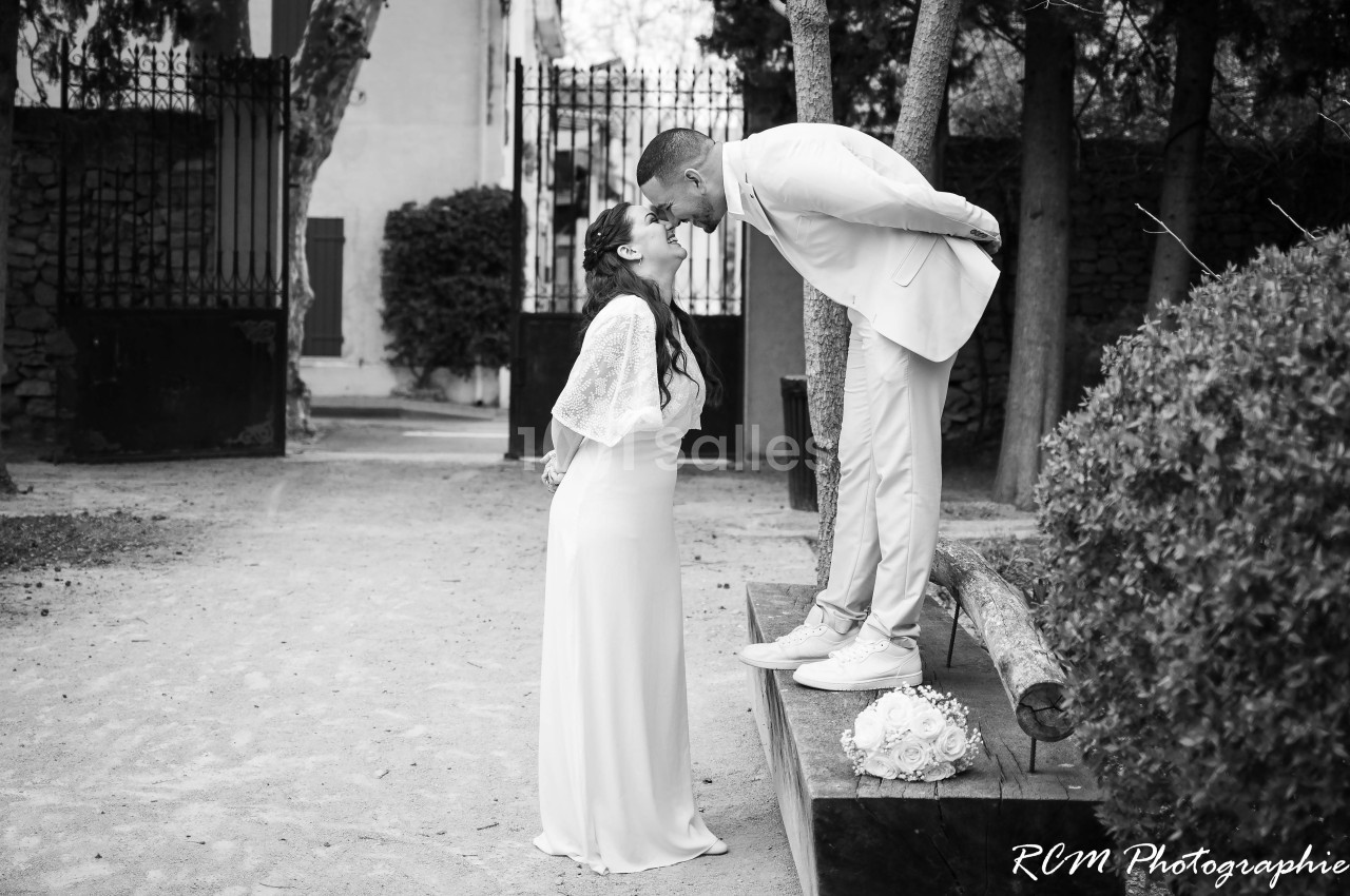 Un couple de mariés échange un moment complice dans un jardin, l'homme debout sur une plateforme embrasse la femme.