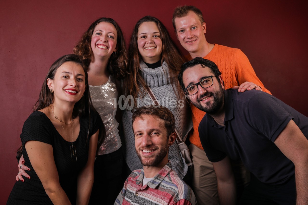 Un groupe de six personnes souriantes posant devant un mur rouge.