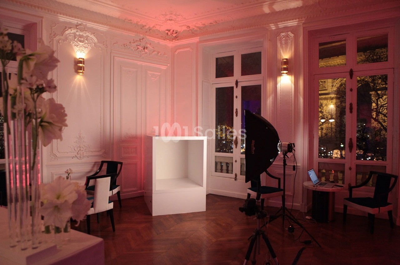 Salle élégante avec moulures, éclairage tamisé rose, équipement photo et grandes fenêtres donnant sur l'extérieur.