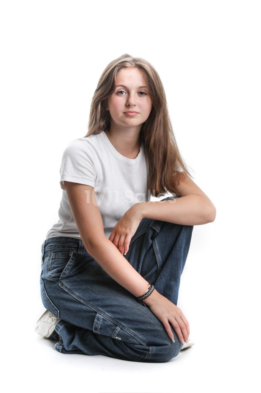 Jeune femme assise sur le sol, portant un t-shirt blanc et un jean, posant devant un fond blanc.