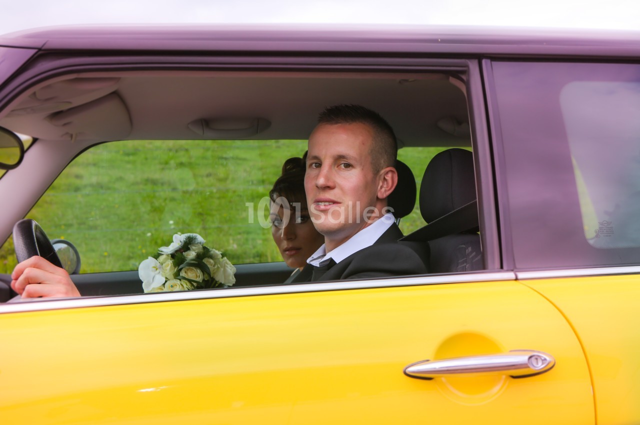 Un couple assis dans une voiture jaune, l'homme au volant et la femme tenant un bouquet de fleurs.