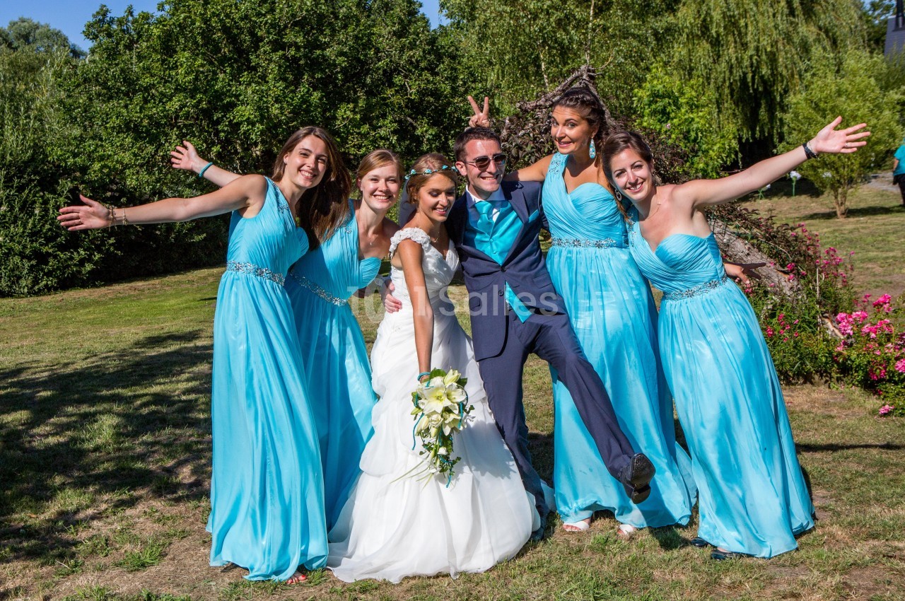 Un couple de mariés souriant entouré de demoiselles d'honneur en robes bleues dans un jardin ensoleillé.