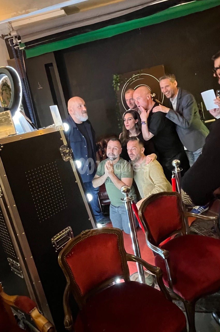 Des personnes posent ensemble devant un photobooth dans un espace intérieur avec des chaises rouges au premier plan.