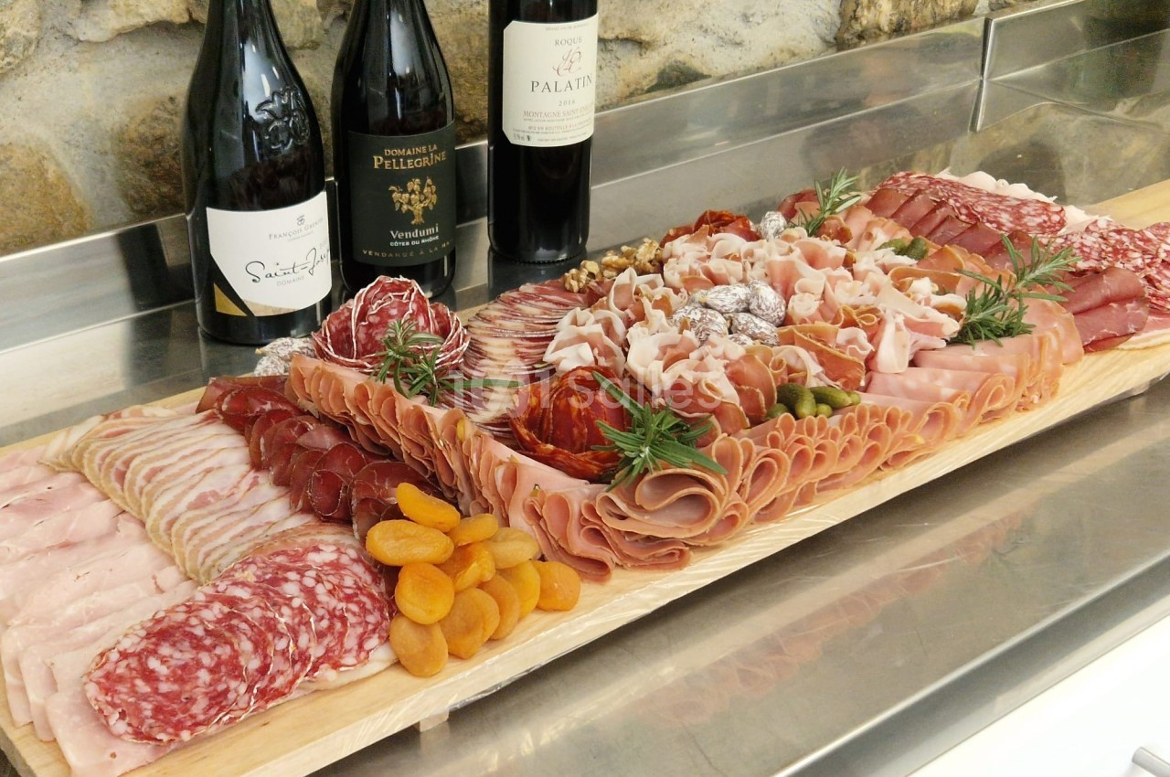Plateau de charcuterie variée avec jambon, saucisson, fruits secs et décoration de romarin, accompagné de bouteilles de vin.