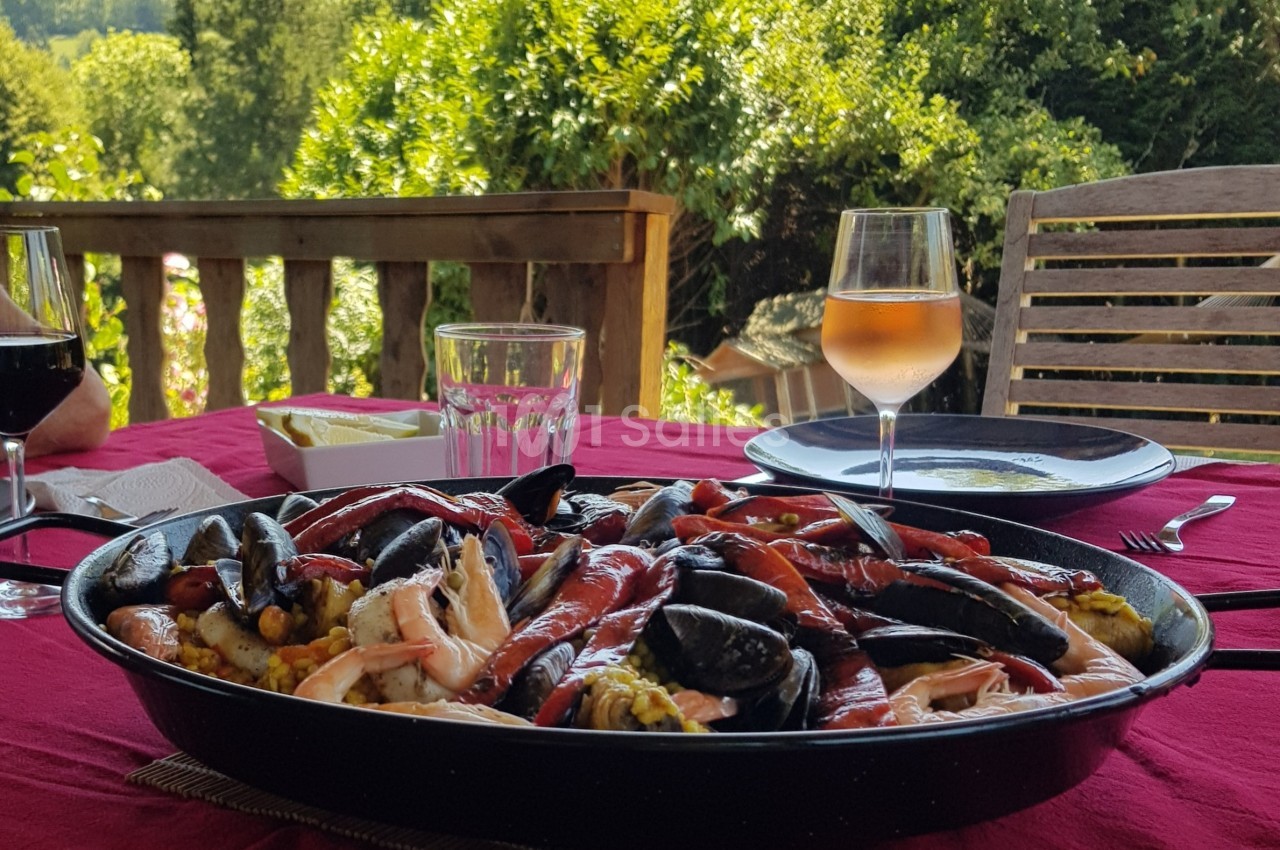 Plat de paella aux fruits de mer servi sur une table en extérieur, accompagné de verres de vin et d'eau.