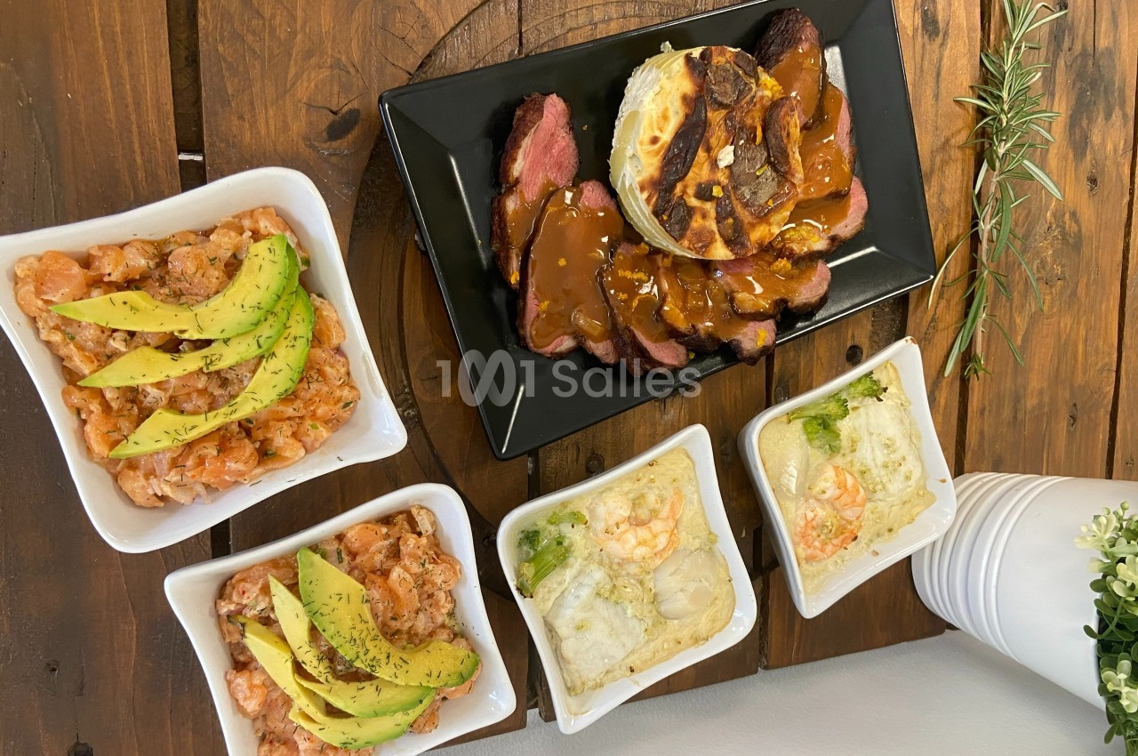 Assortiment de plats comprenant des crevettes à l'avocat, gratins et viande avec sauce, disposés sur une table en bois.