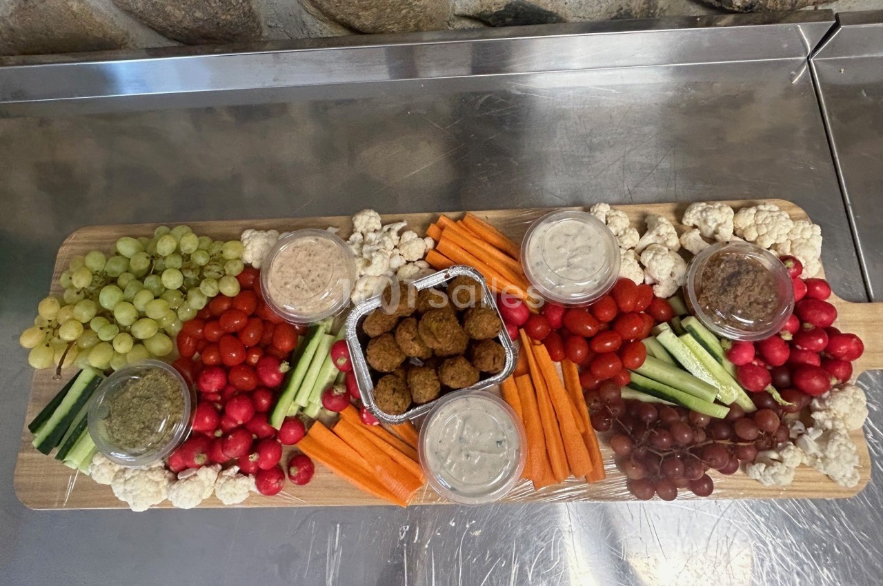 Plateau de légumes frais, raisins, falafels et trempettes disposés sur une planche en bois.