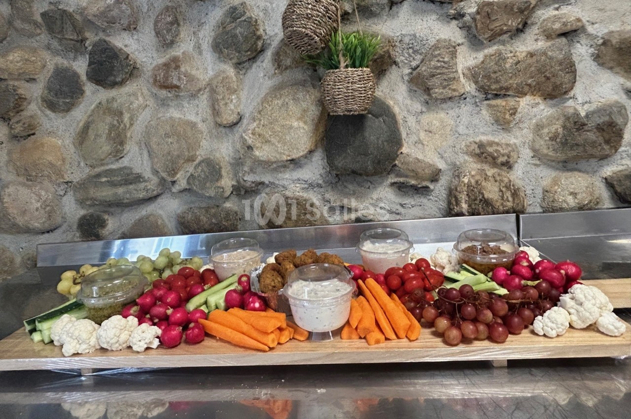 Plateau de légumes frais, fruits et sauces disposés sur une table devant un mur en pierre.