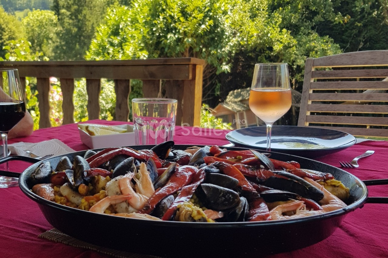 Plat de paella aux fruits de mer servi sur une table en extérieur, accompagné de verres de vin et d'eau.