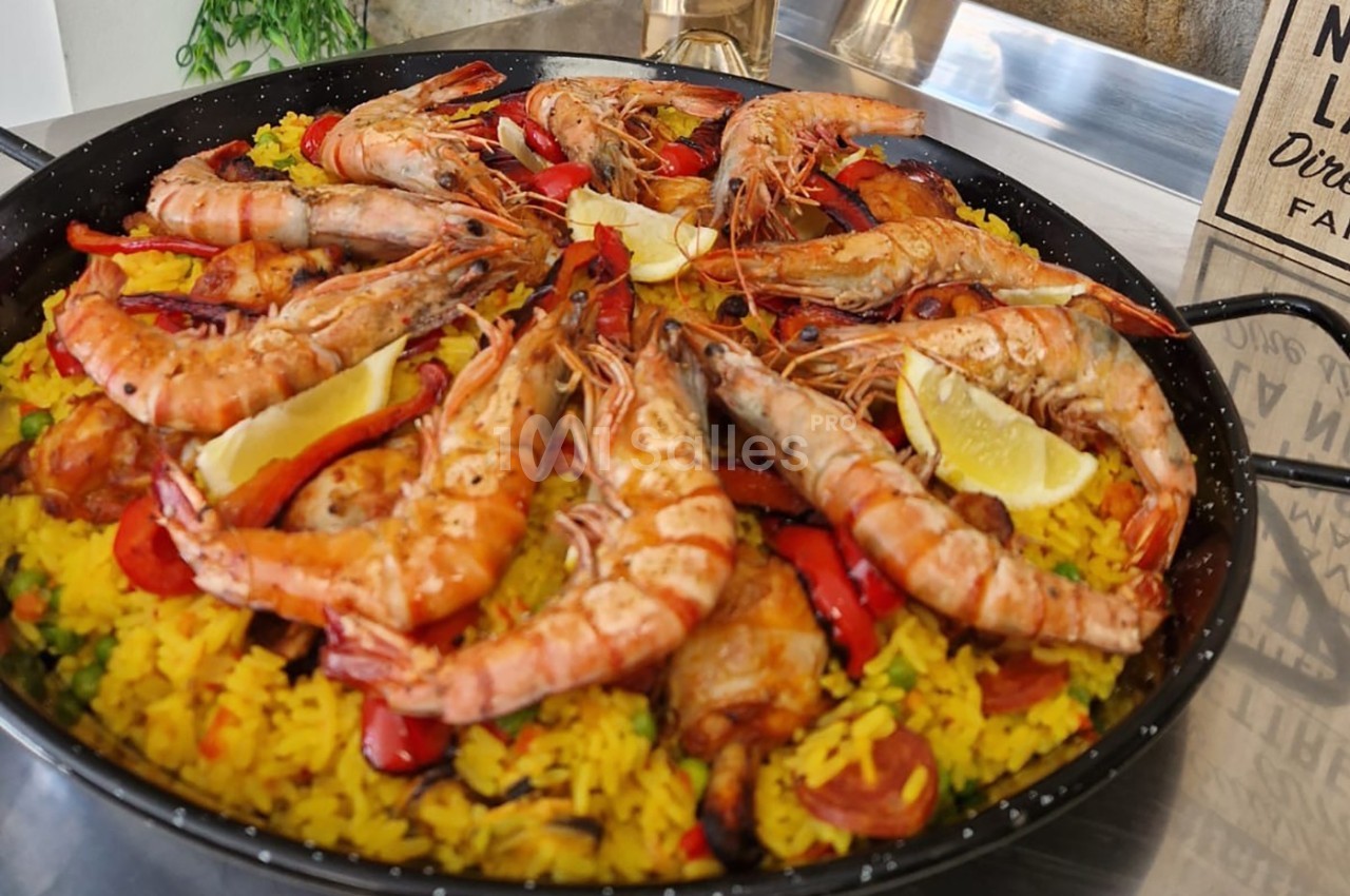 Plat de paella avec crevettes, riz jaune, poivrons rouges, rondelles de chorizo et quartiers de citron.