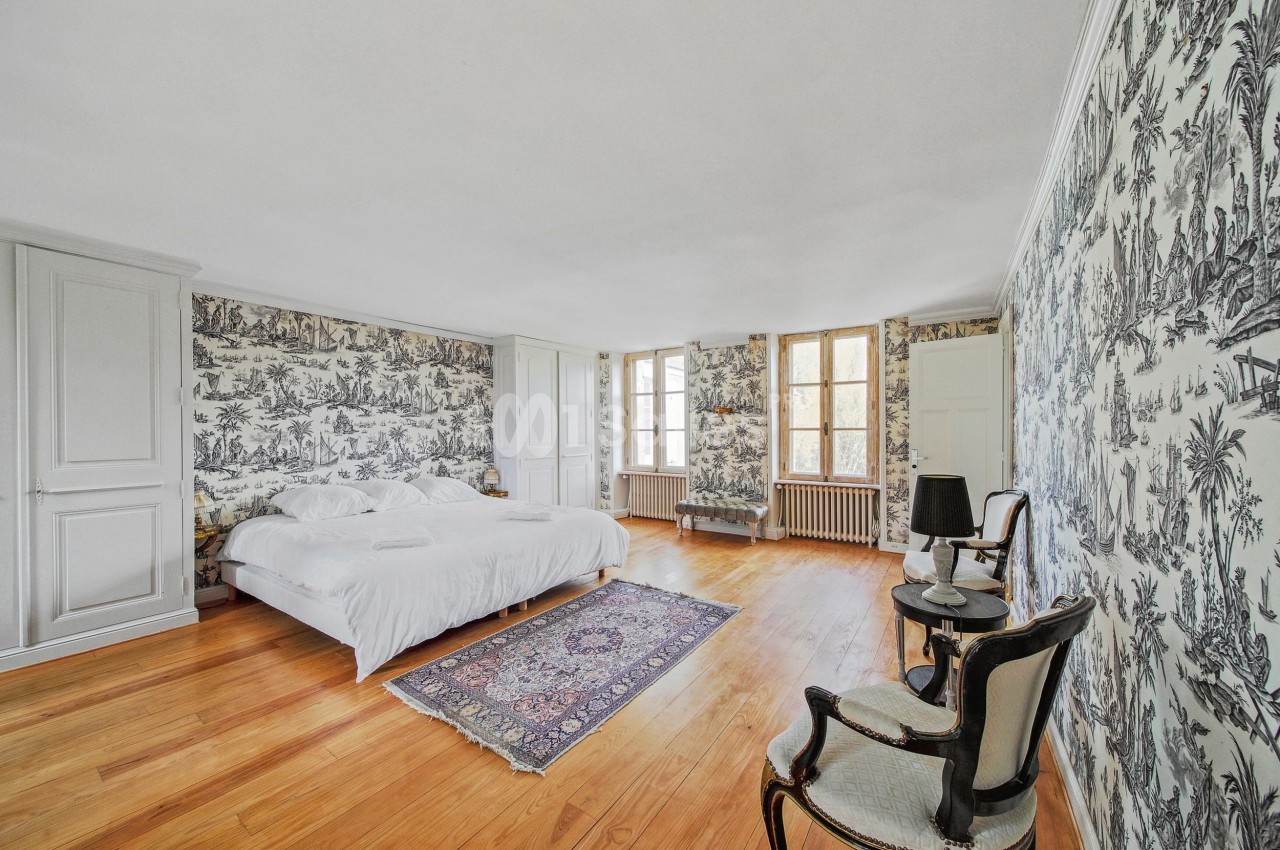 Chambre lumineuse avec lit double, murs ornés de papier peint à motifs, parquet en bois et tapis au sol.
