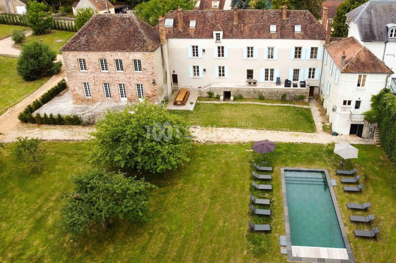 Vue aérienne d'une grande maison ancienne avec jardin, piscine rectangulaire et chaises longues disposées autour.