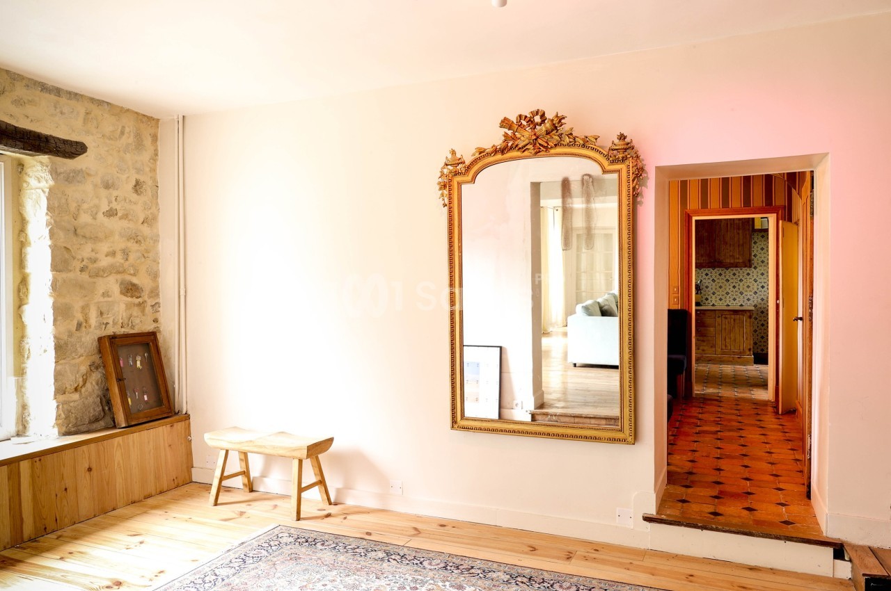 Miroir doré accroché à un mur clair, reflétant une pièce adjacente avec un canapé, dans un intérieur lumineux.