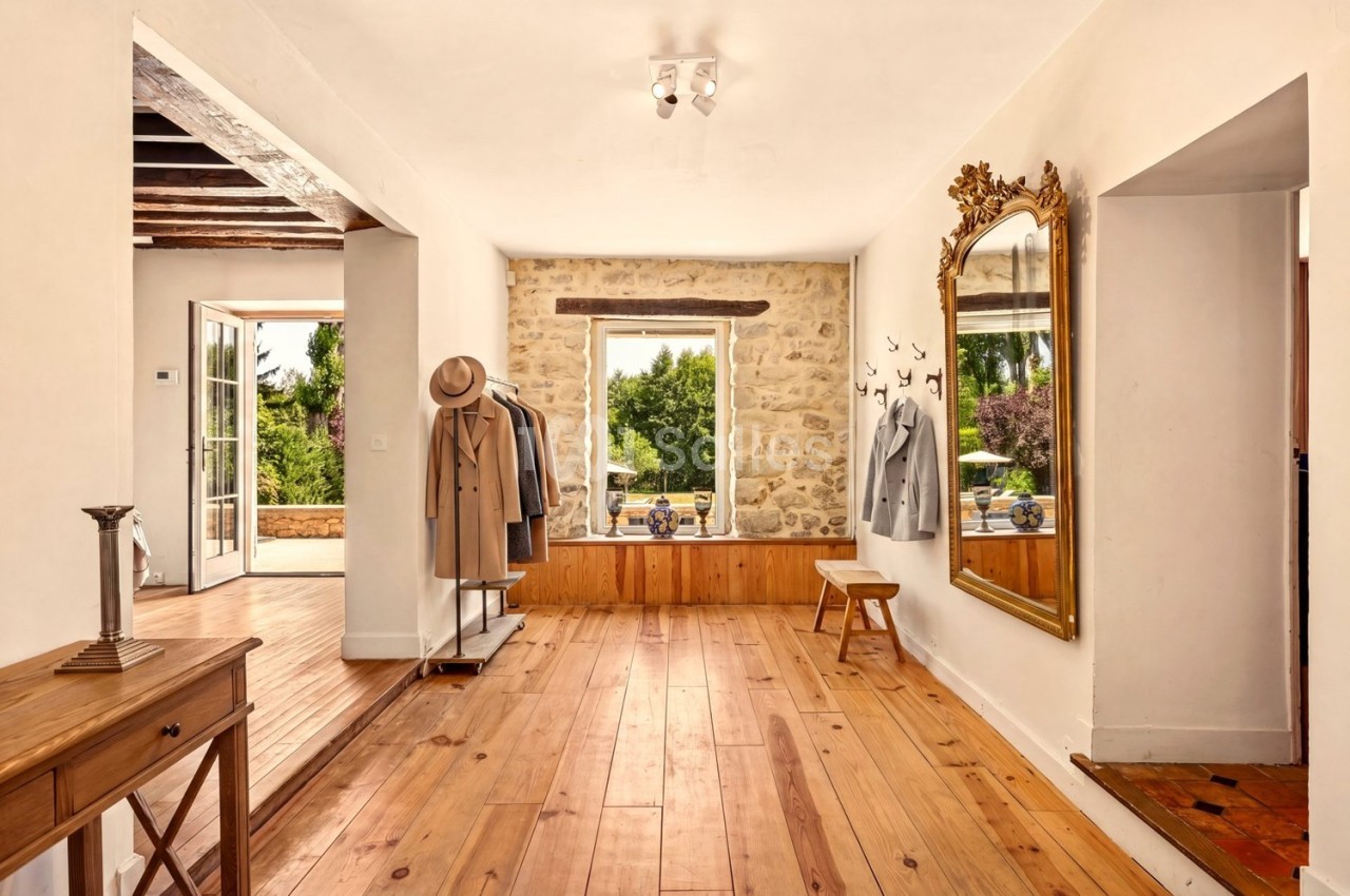 Intérieur lumineux avec parquet, miroir doré, porte ouverte sur jardin et portants avec vêtements.