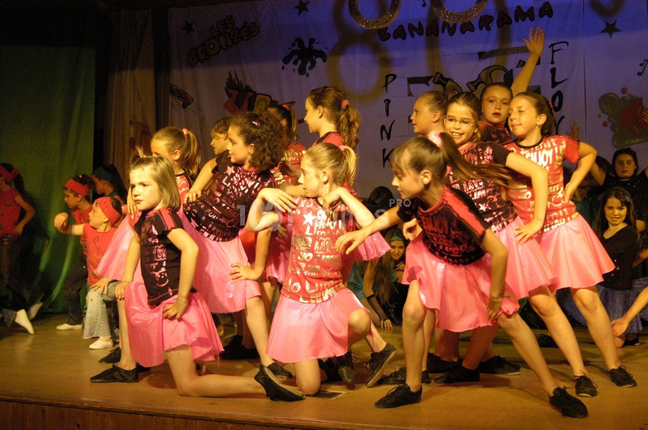 Des enfants en tenue de danse rose et noire exécutent une chorégraphie sur une scène décorée.